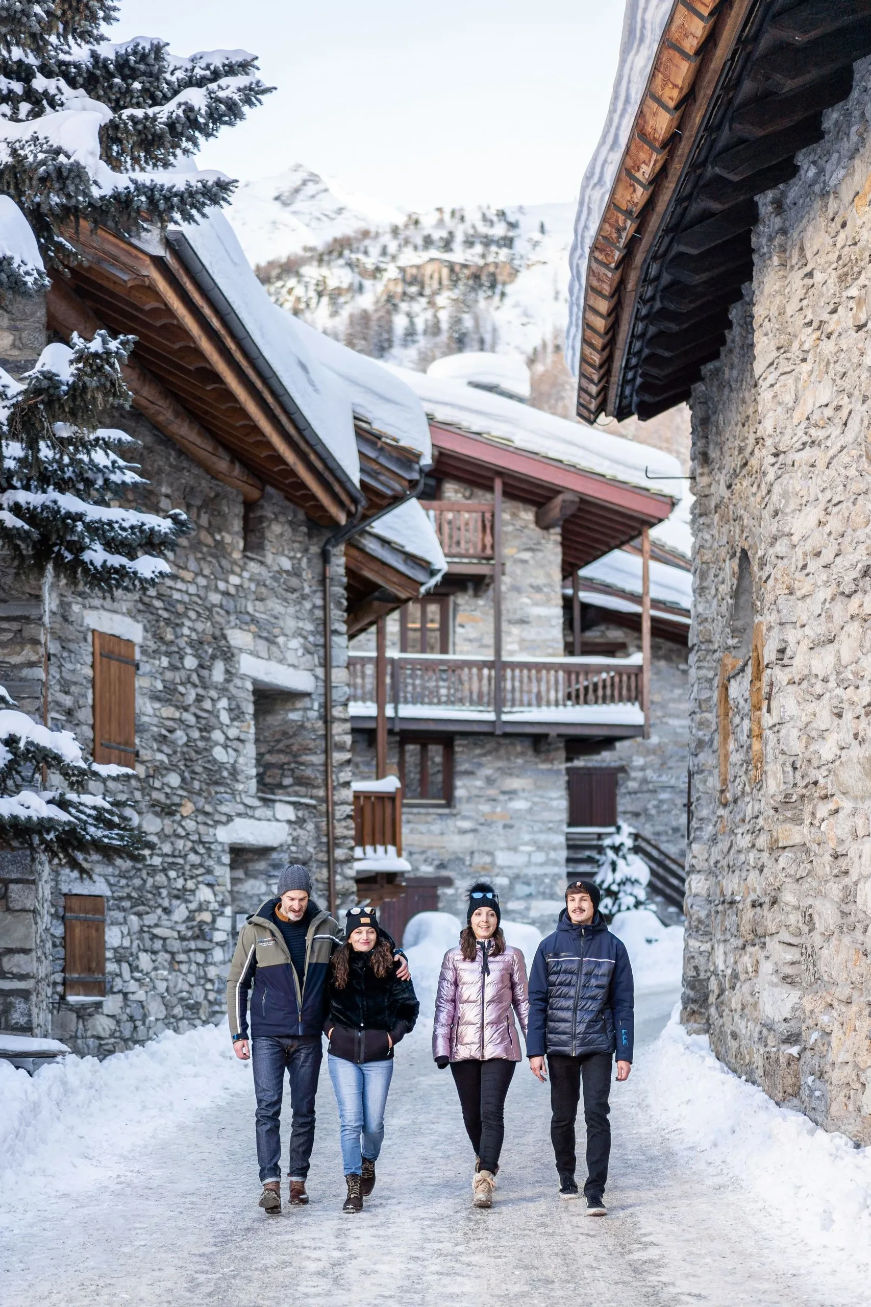 Quatre personnes marchent dans un village enneigé, l'hôtel Village La Mourra pour un séjour à Val d’Isère