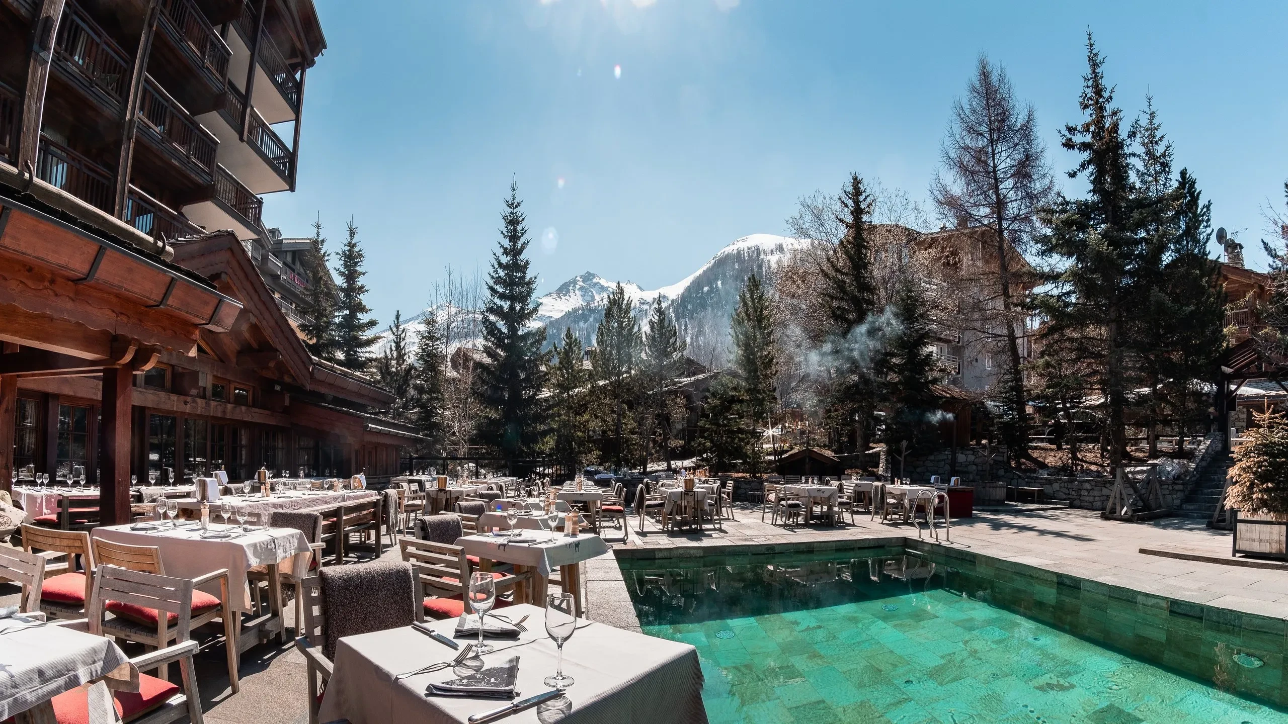 Terrasse en montagne avec piscine et tables dressées.